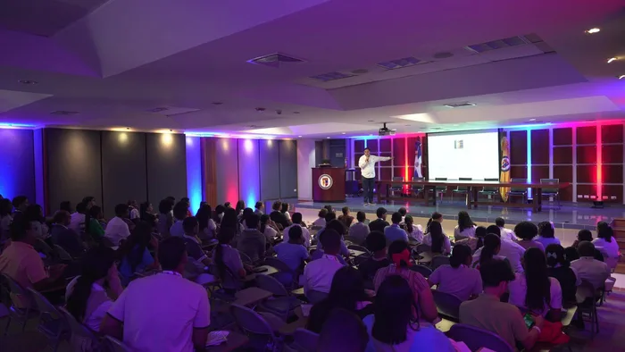 Jean Frías on stage in the PUCMM auditorium in Santiago, in front of a full room of students